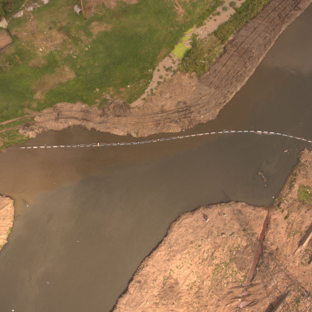 Aerial view of an AlphaMERS floating trash barrier across a river